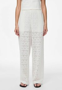 Pantalons blancs à motifs avec une coupe ample, présentant des designs à œillets et une silhouette à jambes larges, complétés par une taille élastique.