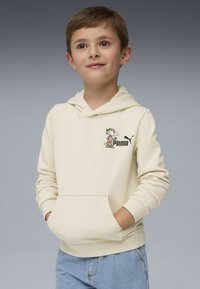 Felpa crema con tasca a marsupio, con un personaggio dei cartoni animati colorato e un logo Puma nero sul petto. Indossata con jeans azzurri chiari.