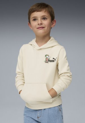 Cremiger Hoodie mit einer Kängurutasche, der ein farbenfrohes Cartoon-Motiv und ein schwarzes Puma-Logo auf der Brust hat. Getragen mit hellblauen Jeans.
