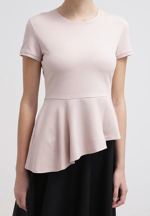 Vrouw draagt een lichtroze top met korte mouwen en een asymmetrische peplumzoom, gecombineerd met een zwarte rok.
