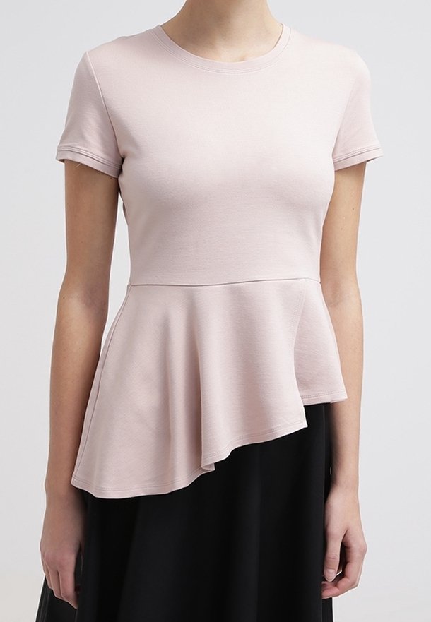 Femme portant un haut rose pâle à manches courtes avec un ourlet peplum asymétrique, associé à une jupe noire.