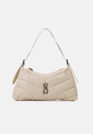 Beige doorgestikte schoudertas met een enkele riem en metalen logodetail aan de voorkant in het midden tegen een effen achtergrond.