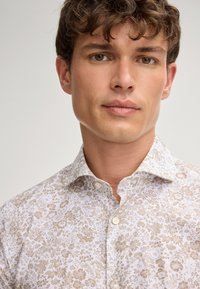 Weißes Hemd mit Knopfleiste, das ein detailliertes florales Muster in Hellbraun zeigt. Entworfen mit einem klassischen Kragen und einer weichen Stofftextur.