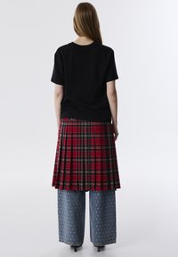 Zwart katoenen T-shirt, rood geruit plooirokje en wijde spijkerbroek versierd met zilveren studs. Eenvoudig achteraanzicht, minimale achtergrond.