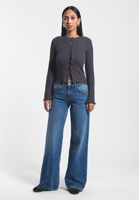 Top gris de manga larga con relieve y botones en forma de escallola, combinado con unos jeans de pierna ancha de talle alto en azul, con costuras clásicas y bolsillos.