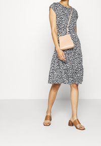 Kvinna i en svart och vit leopardmönstrad klänning, beige klacksandaler och bär en liten ljusrosa axelväska.