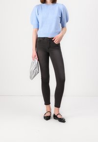 Jasnoniebieski sweter z krótkim rękawem wykonany z miękkiego materiału, zestawiony z ciemnoszarymi obcisłymi dżinsami z wysokim stanem oraz czarnymi balerinami z ozdobnymi ćwiekami.