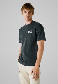 Mørkegrå bomulds T-shirt med et hvidt "Red Bull RACING" logo på venstre bryst, med rund hals og korte ærmer.