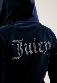 Marineblauwe velours hoodie met een strass "Juicy" logo op de achterkant, met een zachte textuur en een kangoeroezak aan de voorkant.