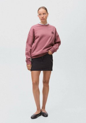 Dunkelpinkes Sweatshirt mit Rundhalsausschnitt und Logodetails, kombiniert mit einem schwarzen Denim-Minirock mit Seitentaschen und silbernen Beschlägen. Schwarze Ballerinas.
