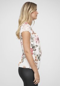 Bloes met bloemmotief en korte kanten mouwen, met een lichte achtergrond en kleurrijke bloemen. Iets losse pasvorm, gecombineerd met zwarte legging.