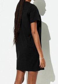 Abito t-shirt nero con maniche corte, vestibilità ampia e design fino al ginocchio. Tessuto di cotone liscio. Stile minimalista senza motivi visibili.