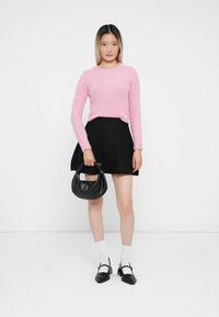 Rosa fluffy genser, svart flaretskjørt, hvite sokker og svart håndveske. Svart sko med firkantet tå og stropp. En enkel, sammenhengende stil.