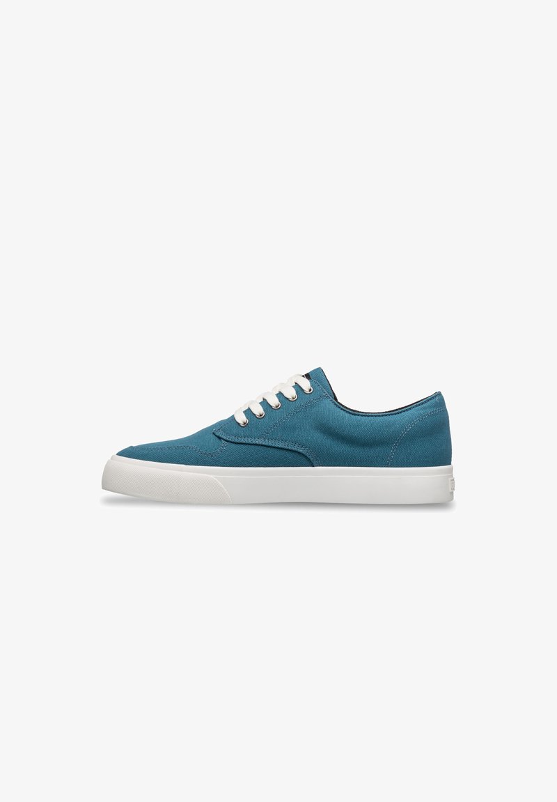 Low-top sneaker van teal canvas met witte veters en dikke witte rubberen zool, zijaanzicht op een witte achtergrond.