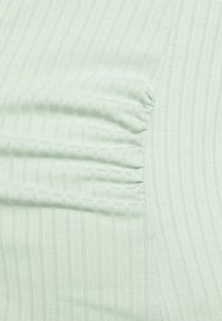 Tecido ribbed verde claro com listras verticais sutis; apresenta um detalhe de costura franzida de um lado. Textura suave.