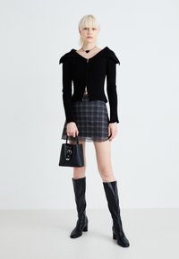 Musthave mustriba kašmiri, millel on lai krae, on kihiline plaaditud mini seeliku peal. Aksessuaarideks on väike must käekott ja põlvekõrgused mustad saapad.