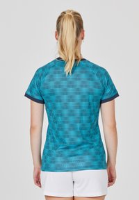 Teal atletisk tröja med ett texturerat mönster och horisontella linjer, marinblå kant på ärmarna, och kombinerad med vita shorts.