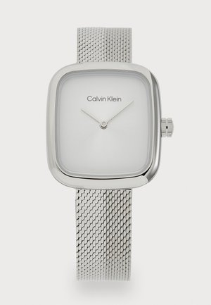 Montre à bracelet en maille argentée avec un boîtier carré. Dotée d'un cadran blanc minimaliste avec deux aiguilles argentées et le logo "Calvin Klein". Design épuré.