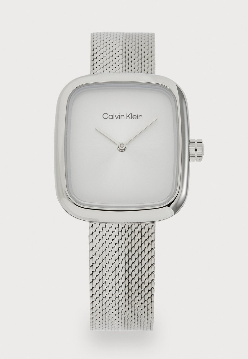 Montre à bracelet en maille argentée avec un boîtier carré. Dotée d'un cadran blanc minimaliste avec deux aiguilles argentées et le logo "Calvin Klein". Design épuré.