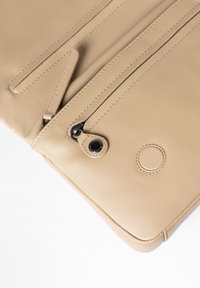 Borsa in pelle beige con due scomparti con zip, texture liscia e dettagli di cucitura sottili. Presenta un accento hardware rotondo.