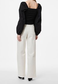 Haut noir à manches bouffantes avec détails froncés et pantalon crème taille haute à jambes larges, associé à des chaussures noires à talons carrés épaisses.