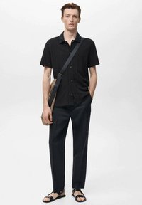 Zwart kortom mouwige overhemd, zwarte rechte broek, zwarte sandalen en een bruine schoudertas zorgen voor een monochrome look.