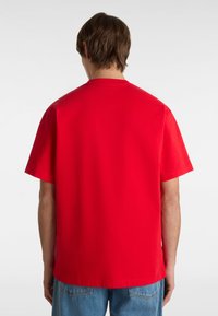 Camiseta de algodón roja con cuello redondo y mangas cortas, que presenta un diseño sencillo y una textura suave, vista desde la parte posterior.