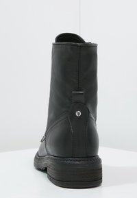 Bottine en cuir noir avec un bout arrondi, un détail de couture, une languette de traction et un accent argenté près du talon. Semelle texturée pour une meilleure adhérence.