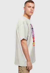 Lysegrå bomulds T-shirt med korte ærmer og farverig tegneserie grafik på fronten. Løs pasform, rund halsudskæring og synlige sømme.
