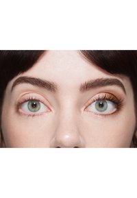 Nærbillede af øjne; venstre øje har naturlige vipper uden makeup, højre øje har gyldent øjenskygge og længere vipper. Lys hudtone, mørkt hår.