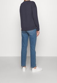 Maglione blu navy con una vestibilità comoda e maniche lunghe, abbinato a jeans a gamba dritta blu chiaro. Sneakers bianche, design minimalista.
