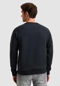 Donker marineblauwe fleece sweatshirt met een ronde hals, ribbelboorden en zoom, en zichtbare naaddetails, gedragen met grijze jeans.