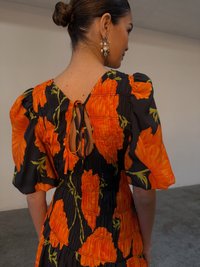 Abito nero con grande motivo floreale arancione, maniche a sbuffo, corpetto arricciato e schiena aperta con chiusura a fiocco.