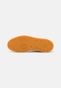 Semelle de chaussure en caoutchouc couleur chewing-gum avec des motifs circulaires, une adhérence texturée, et un petit logo de chat sautant près du talon.