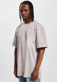 Light gray oversized t-shirt made of soft fabric, featuring short sleeves and embroidered text on the front. Paired with light blue jeans.