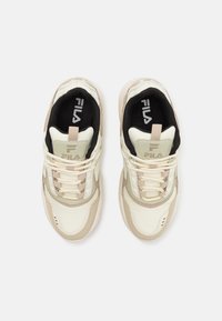 Chaussures de sport crème et beige avec un dessus texturé, bout rond et semelle rembourrée. Comprend le logo Fila et un design à lacets.