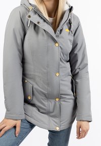 Grå vattentät jacka med huva, gyllene knappar och sidofickor. Har en slät textur och en liten gul paraplylogotyp.