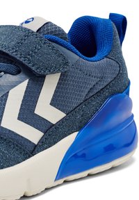 Sneaker z granatową siateczką, białym wzorem w chevron, teksturowanymi akcentami i błyszczącą niebieską podeszwą. W zestawie regulowany pasek na rzep.