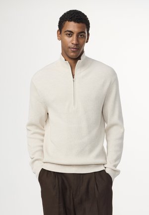 Cremfarbener, gerippter Strickpullover mit einem halben Reißverschluss am Kragen. Merkmale sind lange Ärmel und ein taillierter Saum. Weicher Stoff auf schlichtem Hintergrund.