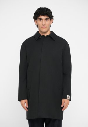 Schwarz coat mit einem strukturierten Kragen, langen Ärmeln, vorderem Knopfverschluss und seitlichen Taschen. Mit einem Logosticker am Bund. Glatte Textur.
