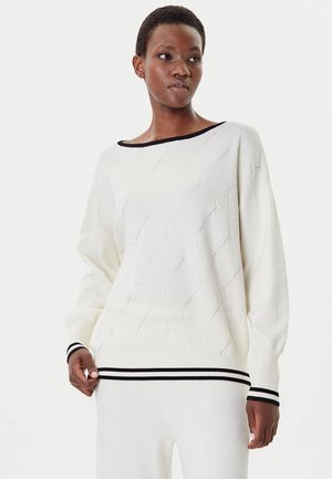 Maglione bianco lavorato a maglia con vestibilità comoda, scollo e polsini neri, e un motivo testurizzato con linee verticali e motivi floreali.