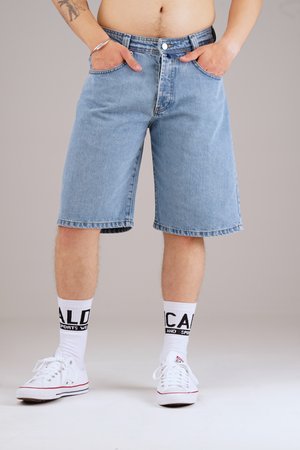 Light blue denim shorts, relaxed fit, knee-length with five pockets. Paired with white sneakers and crew-length socks featuring bold black text.