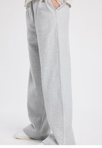 Pantalon de survêtement en coton gris clair avec une coupe décontractée, doté d'un détail de couture latérale festonnée et de poignets légèrement resserrés. Conception axée sur le confort.