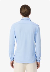 Camisetta azzurro chiaro a maniche lunghe con colletto strutturato, polsini con bottone e una texture liscia; presenta una vestibilità pulita e su misura.