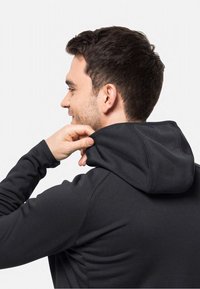 Felpa nera con una texture morbida, dotata di cappuccio aderente e maniche lunghe. Cuciture visibili lungo le cuciture. Il modello sistema il cappuccio.