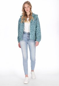 Chaqueta azul verdosa clara con diseño de estampado de leopardo, cierre de cremallera y mangas elásticas, combinada con vaqueros azules de talle alto y zapatillas blancas.