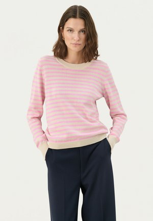 Rosa und creme gestreifter Pullover mit einem gerippten Rundhalsausschnitt und Bündchen, aus weichem Strickmaterial, kombiniert mit dunkelblauen Hosen.