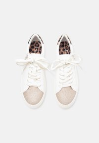 Λευκά αθλητικά παπούτσια με γυαλιστερά χρυσά δάχτυλα και υφασμάτινες εσωτερικές σόλες με λεοπάρ ντεσέν. Διαθέτουν υφασμάτινη επένδυση, στρογγυλή μύτη και επίπεδες κορδόνια.