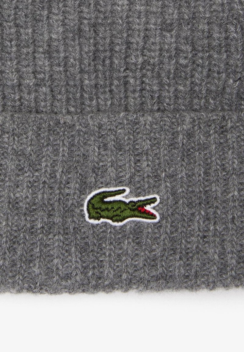 Graue Strickmütze mit vertikalem Rippenmuster. Vorne mit einem grünen gestickten Krokodil-Logo, das in Weiß umrandet ist.