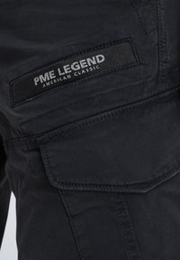 Schwarze Cargo-Hosen mit sichtbaren Nähten, einer Seitentasche und einem Stoffetikett mit der Aufschrift "PME LEGEND AMERICAN CLASSIC." Robustes Material.